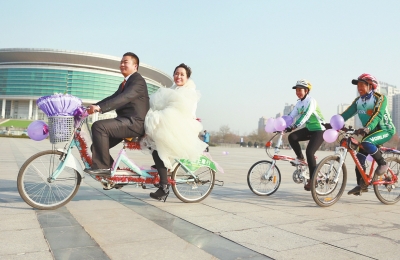 氣球和鮮花裝點(diǎn)的雙人自行車，新郎郝幸福載著美麗新娘回家。