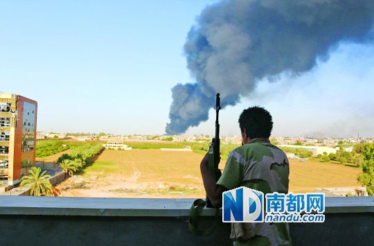 2日，利比亞首都的黎波里，一民兵武裝成員眺望被火箭彈擊中的儲(chǔ)油罐冒出濃煙。
