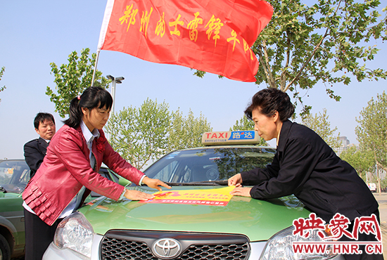 　　授旗結(jié)束后，首都的士雷鋒車隊(duì)王鳳進(jìn)隊(duì)長（右）與鄭州的的哥的姐在車身上貼上標(biāo)識(shí)。