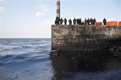昨日，山東青島，清污人員正在海邊清理油污。