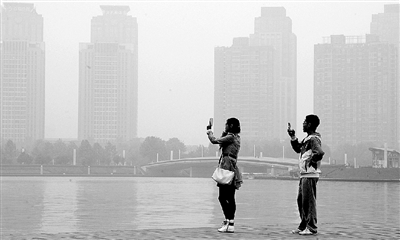 29日中午，鄭東新區(qū)如意湖畔，兩個年輕人拍攝霧霾中的景色。 鄭州晚報記者 馬健 圖