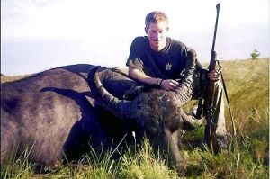 哈里王子手持獵槍，蹲在一頭遭到獵殺的水牛旁邊