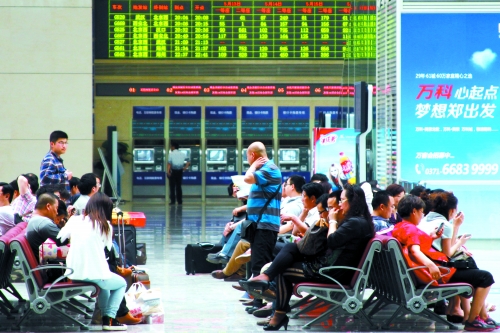 候車大廳溫度很高，一名乘客一手扇風(fēng)、一手擦汗