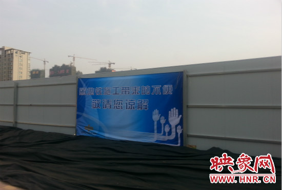 道路南側(cè)圍起了白色的圍擋，墻上標示著“因地鐵施工帶來的不便敬請您諒解”的提示牌。