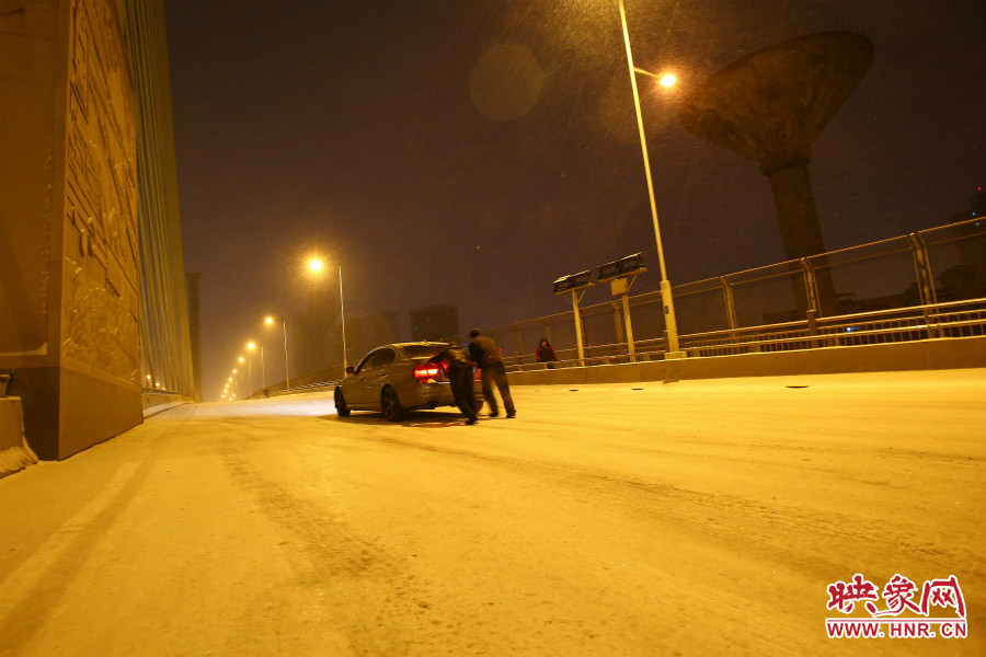 雪天路滑，汽車上橋打滑，兩名“推車人”幫助一輛私家車上坡。