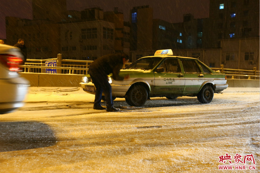 一位出租車司機在車輪前灑上雪，希望能增加輪胎的摩擦力。