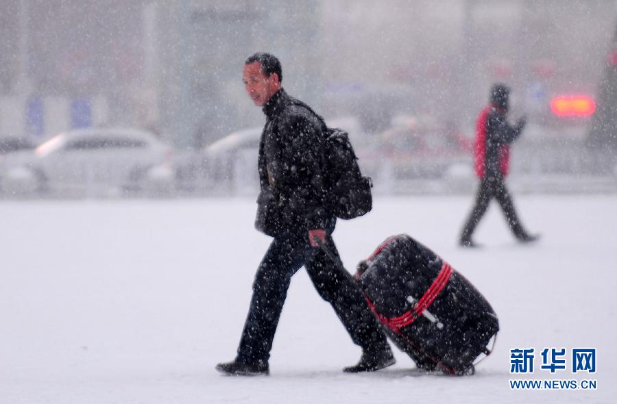 1月19日，旅客冒雪走在沈陽北站站前廣場上。