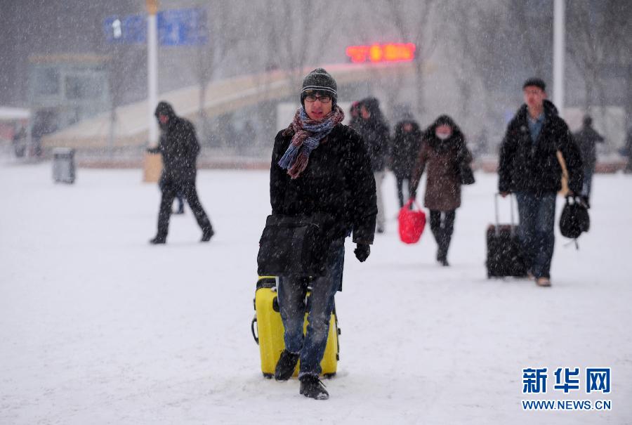 1月19日，旅客冒雪走在沈陽北站站前廣場上。