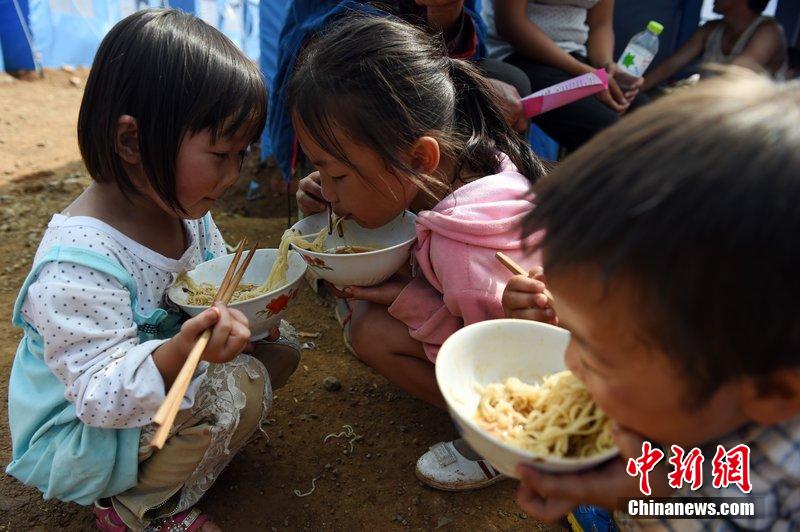 2014年8月6日，云南魯?shù)辇堫^山災(zāi)區(qū)，兒童在帳篷外吃飯。