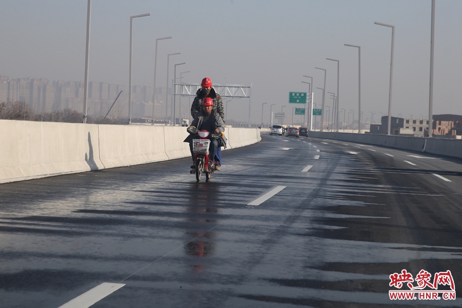 兩名工人騎車經(jīng)過灑水養(yǎng)護路面。