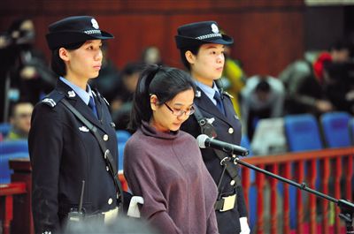 被告人盧梅低著頭，站在朝陽法院刑事審判庭的被告席上。